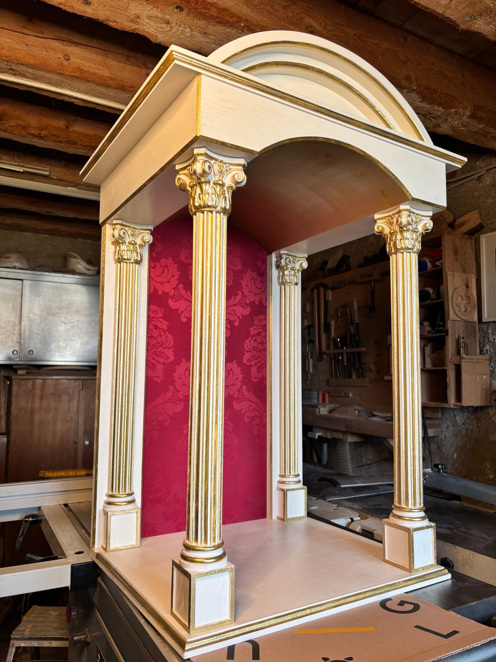 Niche en bois à quatre colonnes cannelées, chapiteaux rehaussés d'or et fond damassé rouge, terminée dans l'atelier.